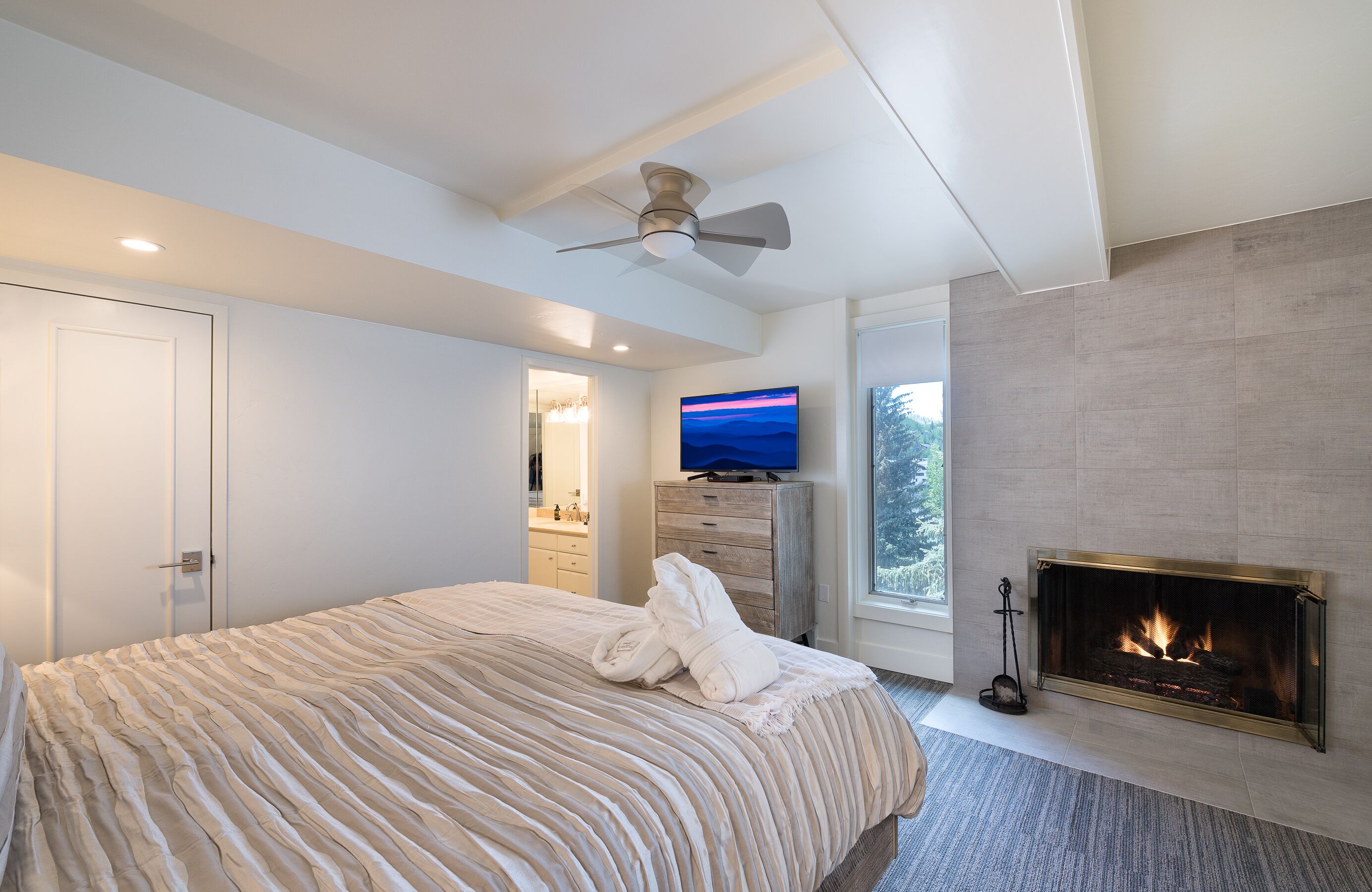 Un dormitorio moderno con una cama grande, televisor, chimenea y ventilador de techo.