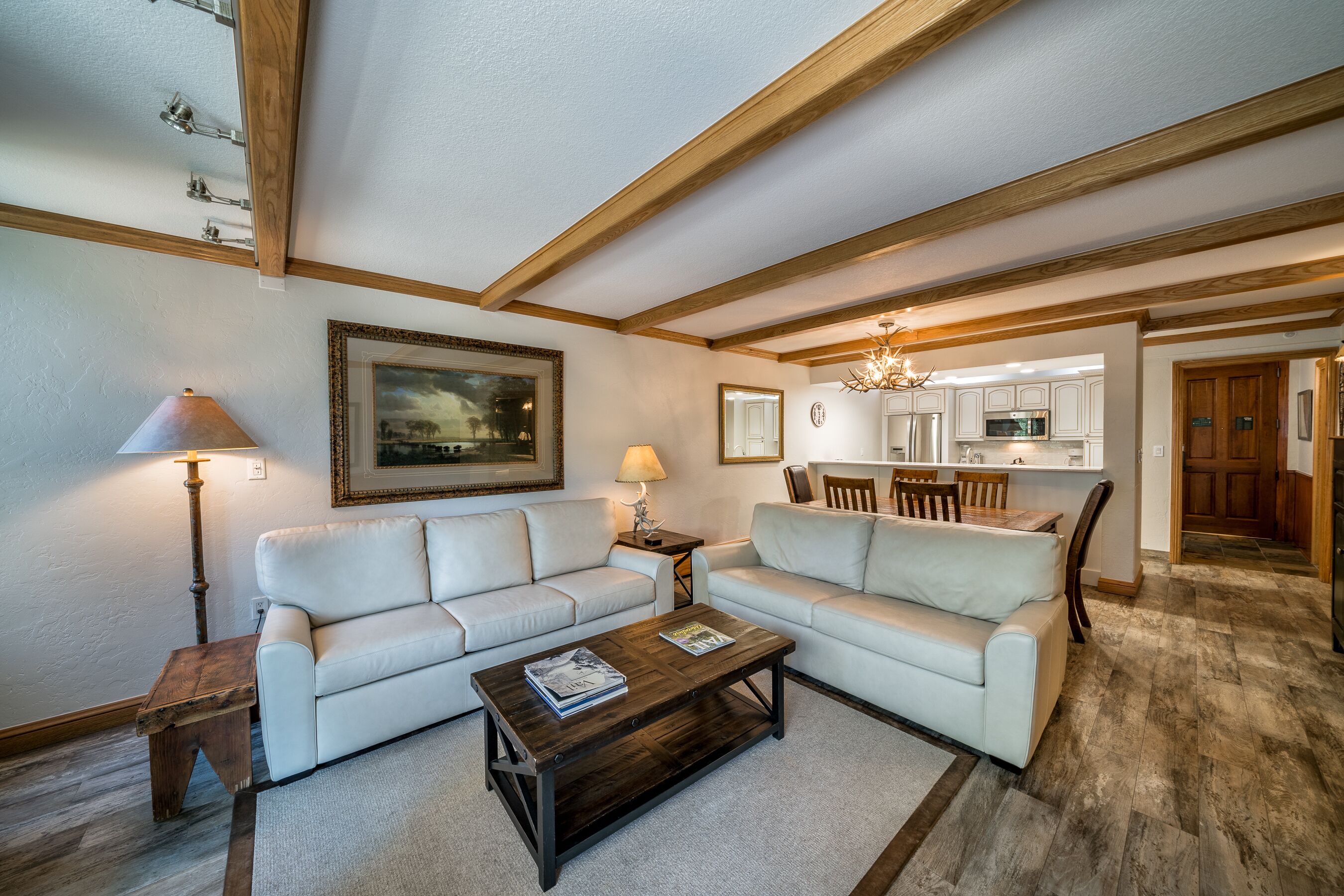 A living room with two white sofas, a wooden coffee table, a lamp, and a painting on the wall.
