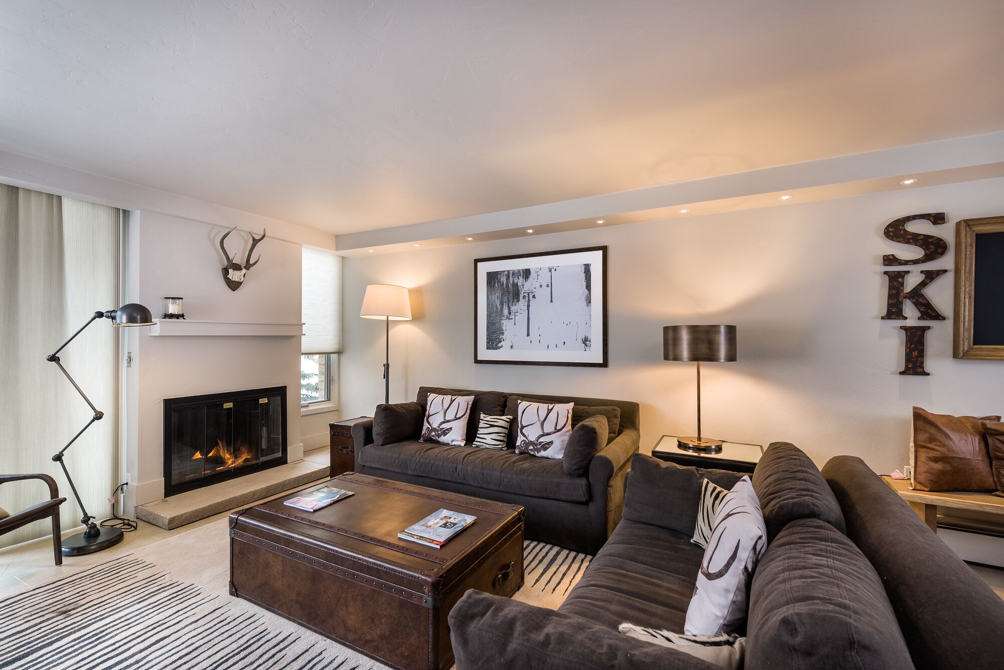 A cozy living room with a fireplace, a sofa set, a coffee table, and a ski-themed decor.