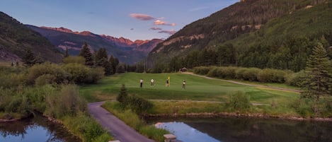 Ein Golfplatz mit Teich, umgeben von Bergen und Bäumen.