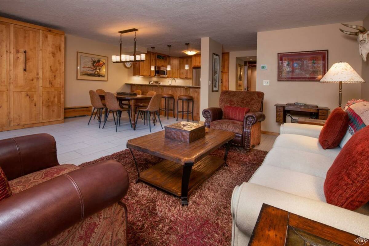 A spacious living room with a large wooden coffee table, leather sofas, and a dining area with bar stools.