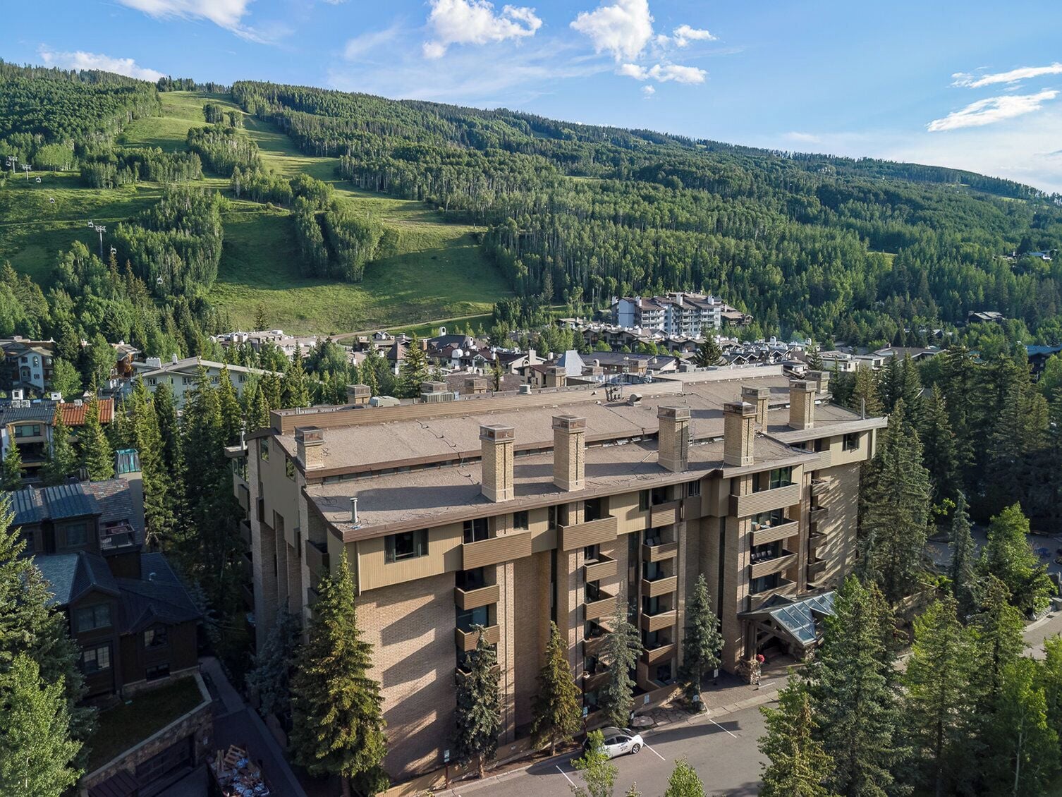 Un edificio de varios pisos con techo plano, rodeado de árboles y un paisaje montañoso.