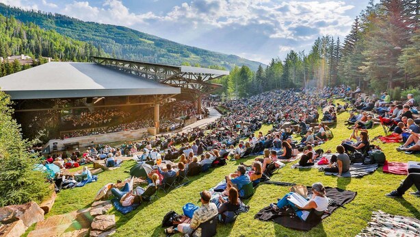 Un anfiteatro al aire libre con escenario y público sentado sobre césped.