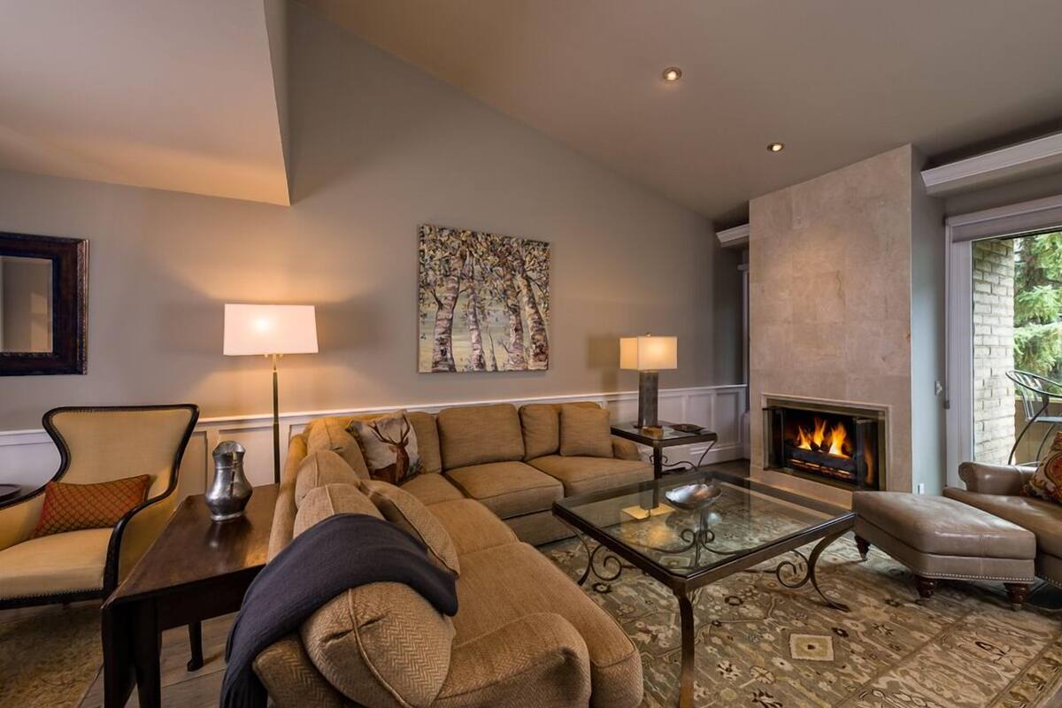 A living room with a sectional sofa, a glass coffee table, a fireplace, and a large painting on the wall.