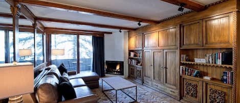 A cozy living room with a fireplace, leather sofa, wooden bookshelves, and a herringbone-patterned floor.