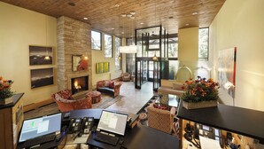 Un vestíbulo amplio con chimenea, varias zonas de estar y un mostrador de recepción con teléfonos y computadoras.