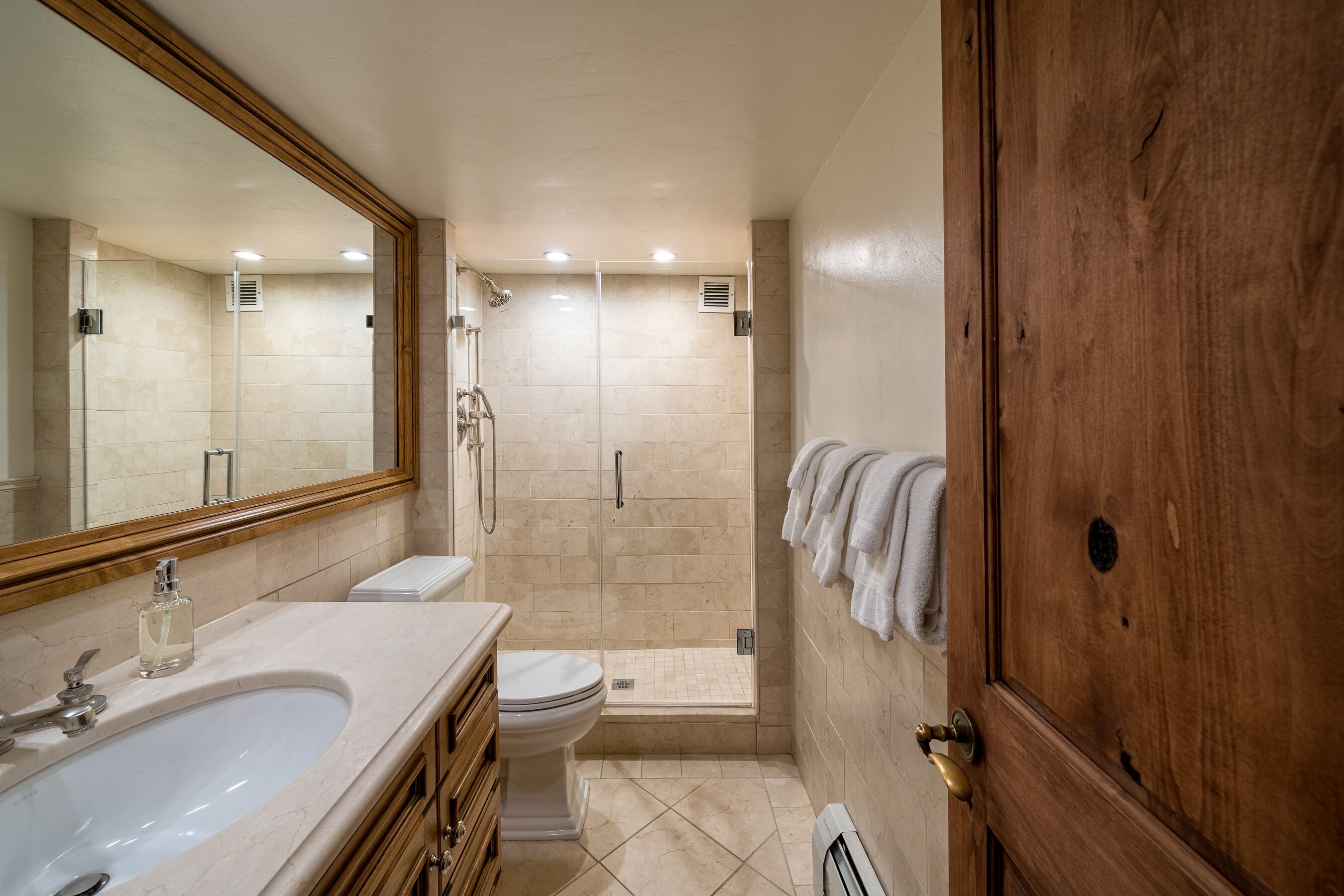 Une salle de bain avec un grand miroir, un lavabo, des toilettes, une douche et une porte en bois.