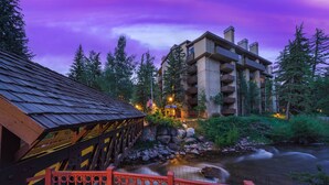 Vista de un hotel a la orilla del río, con un puente de madera y una barandilla roja.