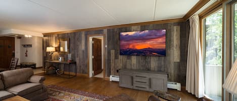 A spacious living room with a large flat-screen TV, leather sofas, a wooden coffee table, and a patterned rug.