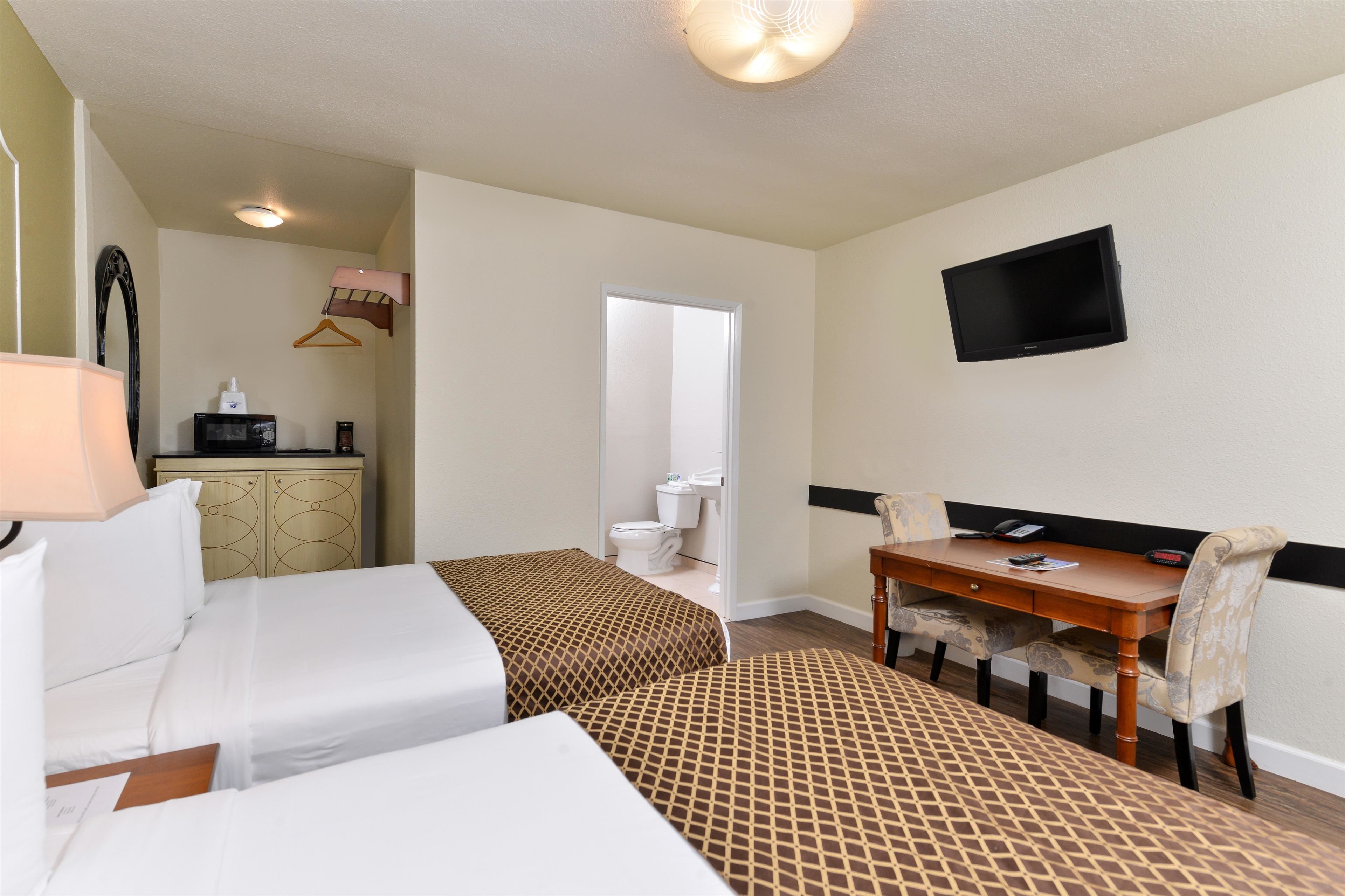 A hotel room with two beds, a desk, a chair, a television, and a bathroom visible through an open door.