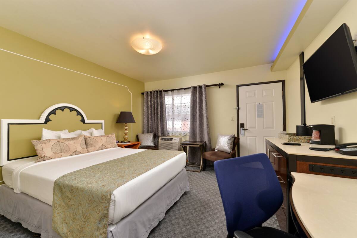 A hotel room with a bed, desk, chair, TV, and window with curtains.