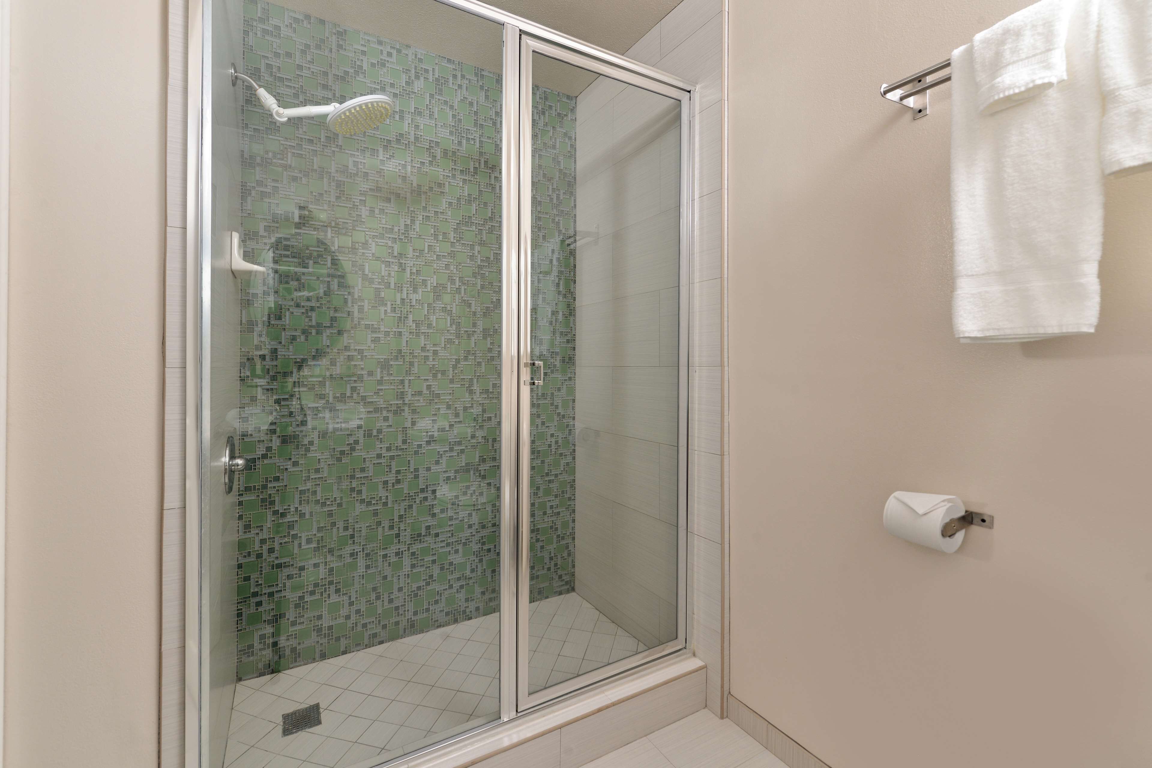 Une douche avec une porte en verre, un mur carrelé et un porte-serviettes avec des serviettes.