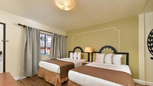 A hotel room with two beds, a wooden floor, a window with curtains, and a wall decoration. - Americas Best Value Inn Rancho Palos Verdes (Rancho Palos Verdes)