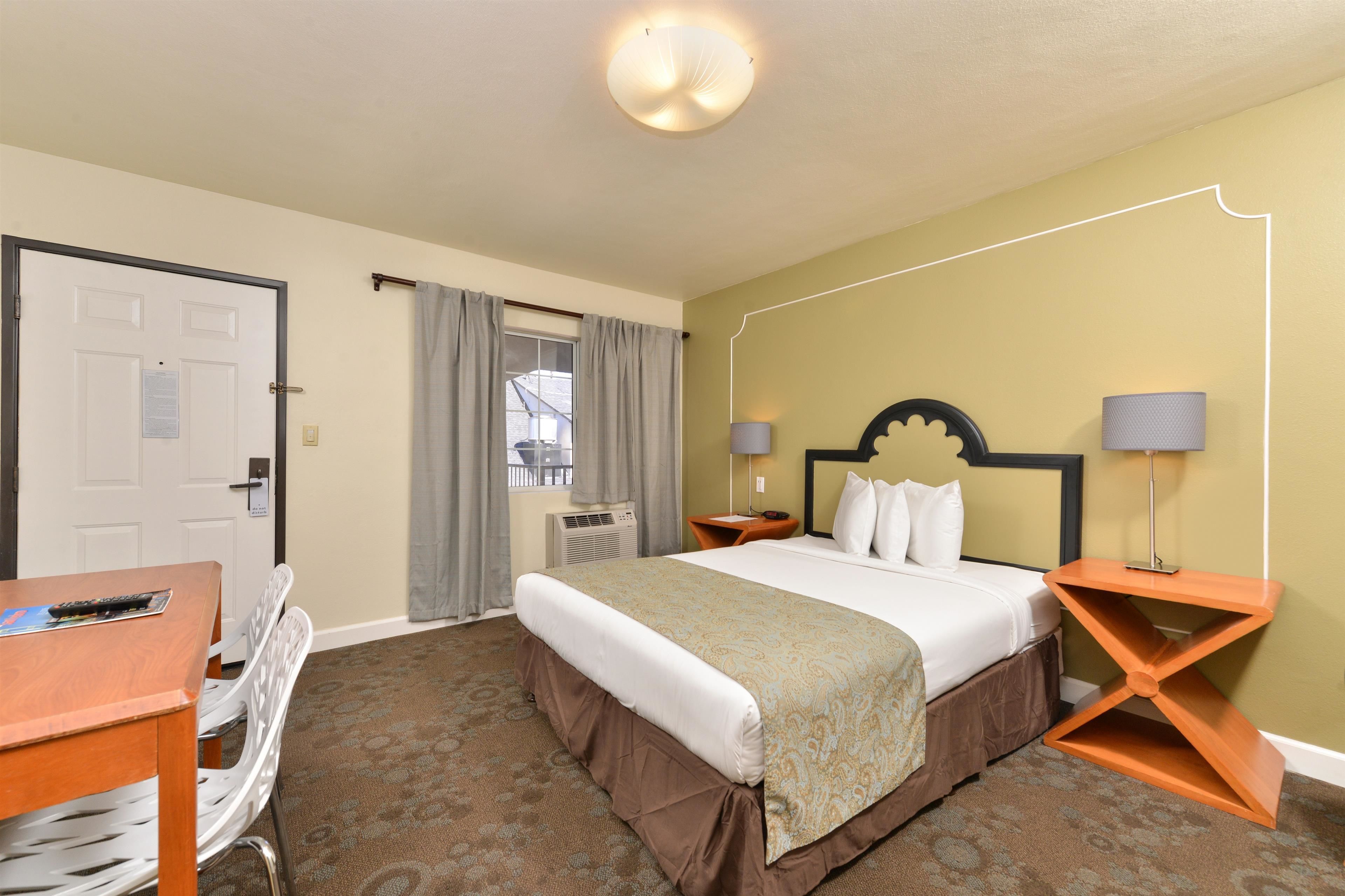 A hotel room with a bed, bedside tables, a desk, and a chair.