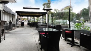 An outdoor patio area with black wicker furniture and red cushions, a covered seating area, and a view of the street and trees. - Americas Best Value Inn Rancho Palos Verdes (Rancho Palos Verdes)
