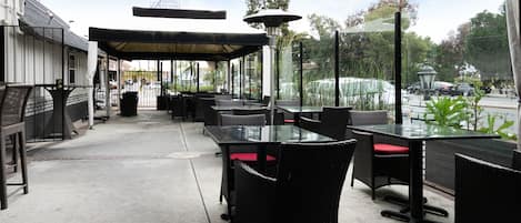 An outdoor patio area with black wicker furniture and red cushions, a covered seating area, and a view of the street and trees.