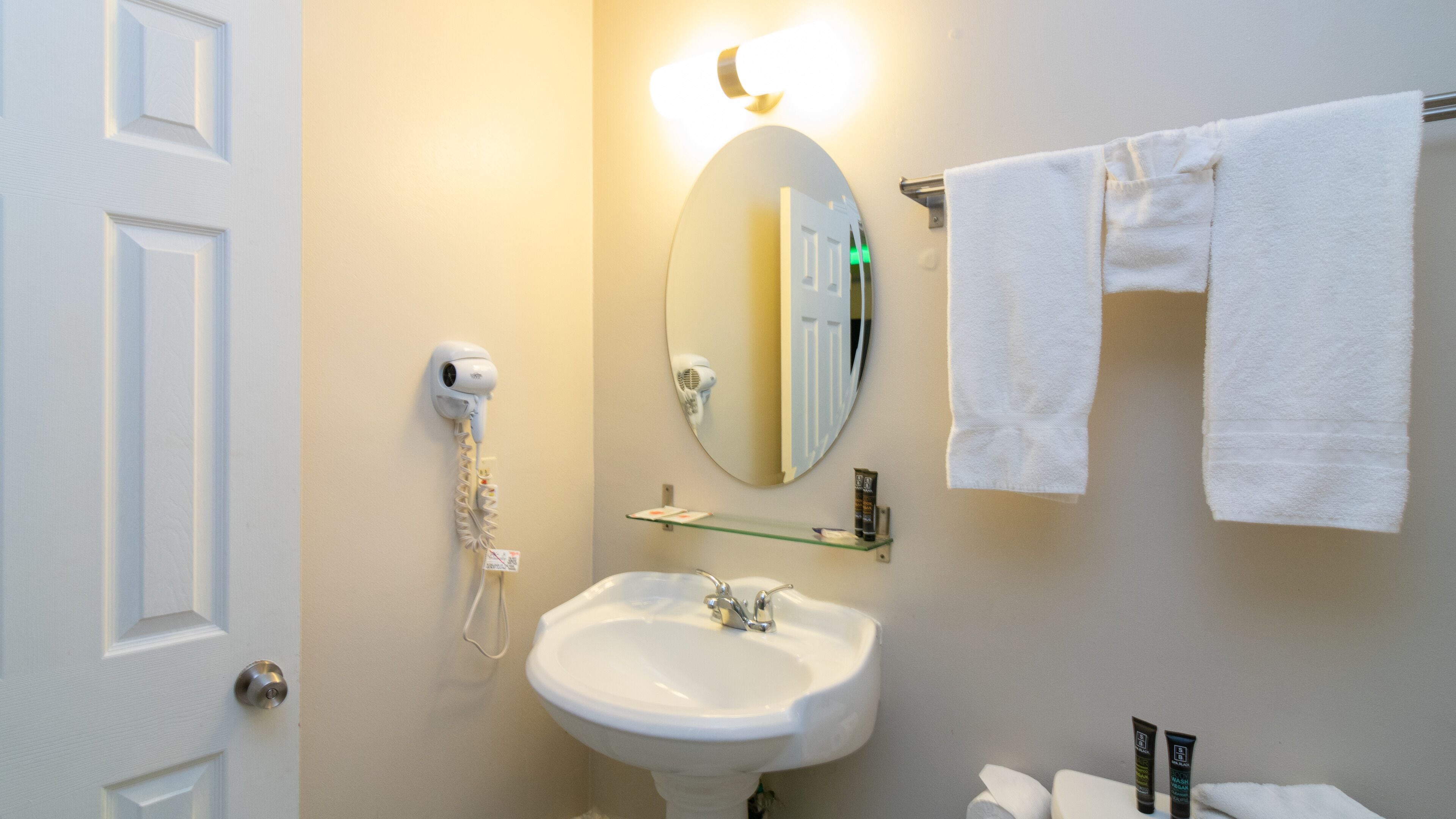 Ein Badezimmer mit einem weißen Waschbecken, einem Spiegel, einem Fön und einem Handtuchhalter.