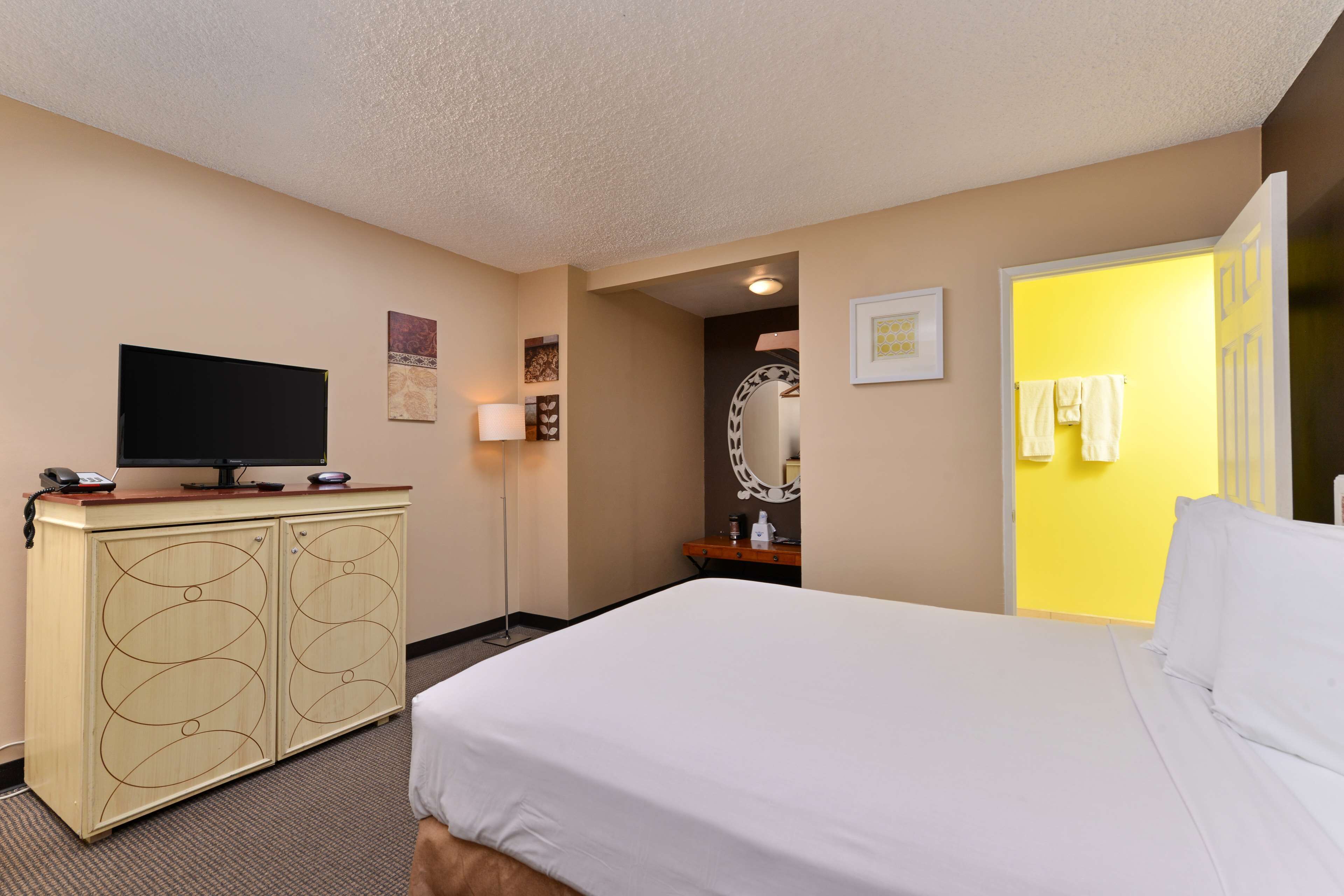 A hotel room with a bed, a television on a cabinet, a bathroom with a yellow door, and a mirror.