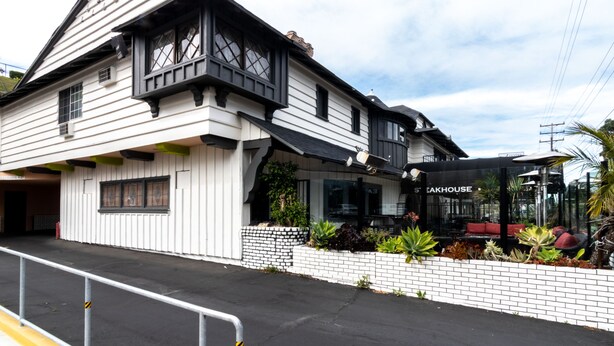 A two-story building with a black and white facade, a visible restaurant named "SAEKHOUSE" with outdoor seating, and a brick planter with various plants. - Americas Best Value Inn Rancho Palos Verdes (Rancho Palos Verdes)