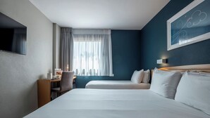 Een hotelkamer met een groot bed, een bureau met stoel, een aan de muur bevestigde televisie en een raam met gordijnen.