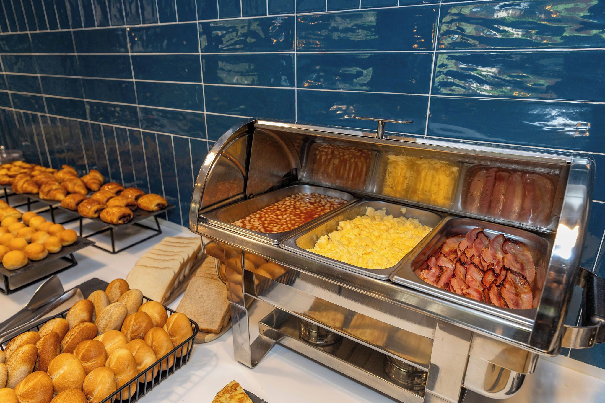 A buffet with various food items including baked goods, beans, eggs, and bacon.