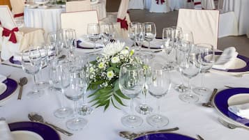 Una mesa de banquete dispuesta con varias copas de vino, platos y cubiertos, rodeada de sillas con lazos blancos y rojos.