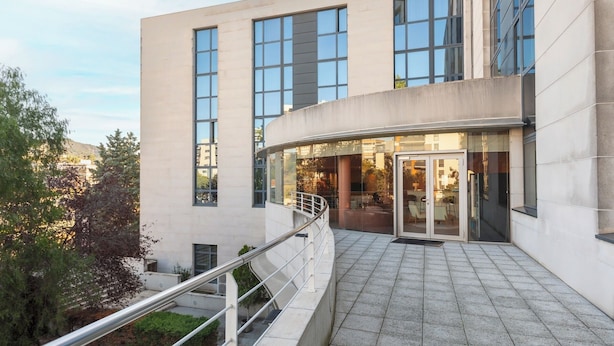 Un bâtiment moderne doté de grandes fenêtres, d’une entrée incurvée et d’un escalier menant à un balcon.