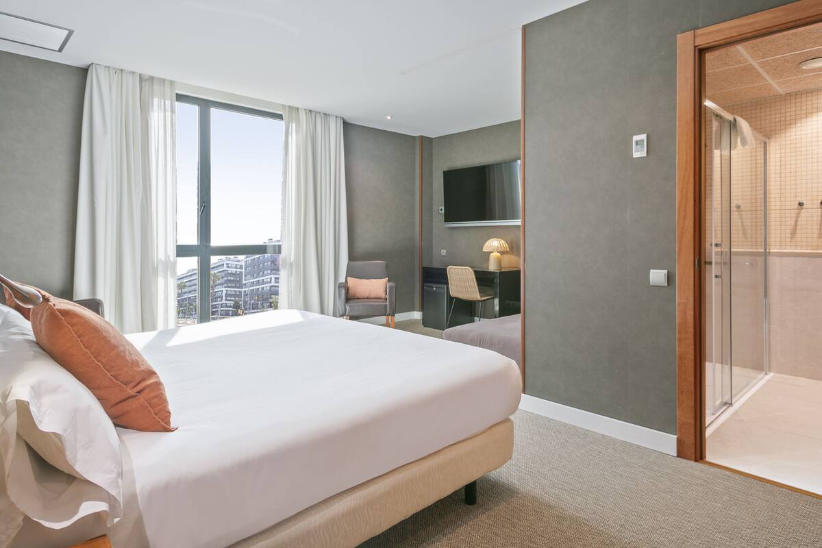 A hotel room with a large bed, a desk with a chair, a TV, and a shower area.