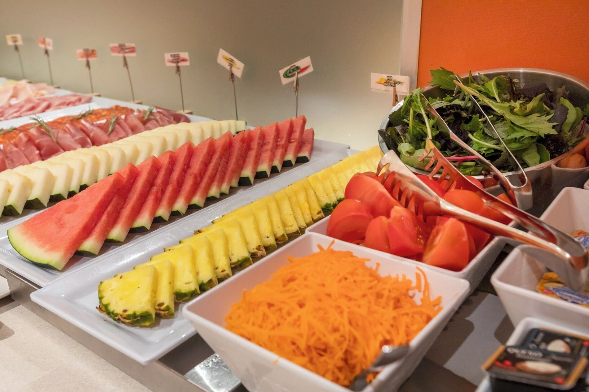 Un bufé con diversas frutas y verduras, entre ellas sandía, piña y zanahorias.