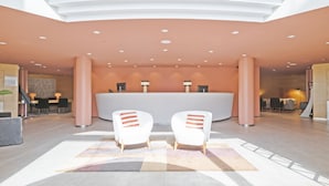 Un espace d’accueil moderne avec un bureau incurvé, deux fauteuils blancs et un tapis à motifs.