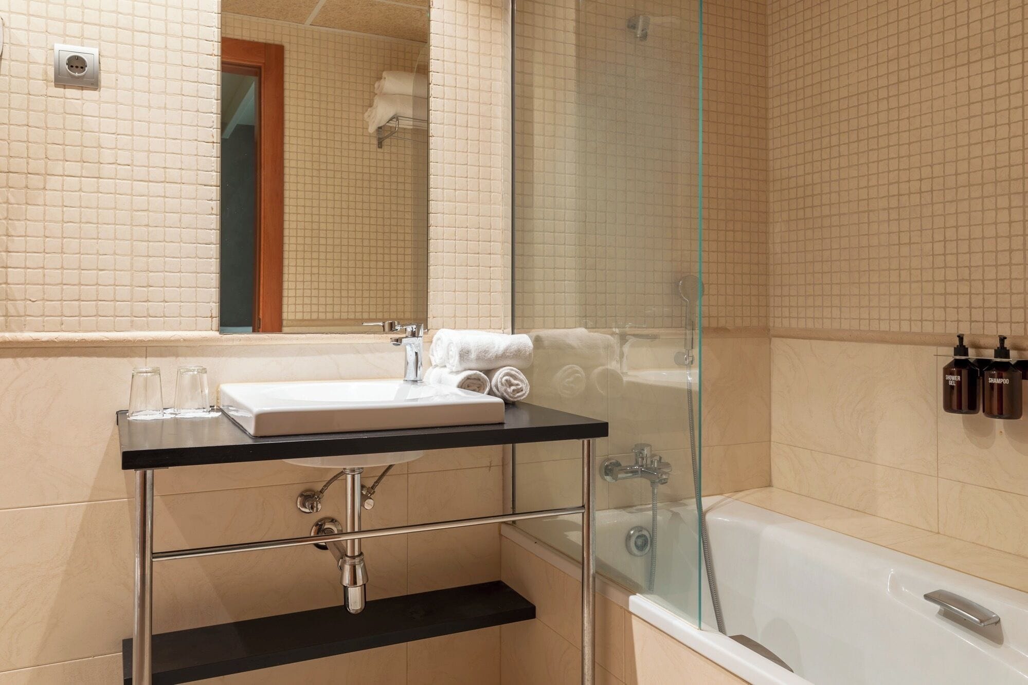 Een moderne badkamer met een douchecabine van glas, een wastafel met een zwart aanrechtblad en een spiegel boven de wastafel.
