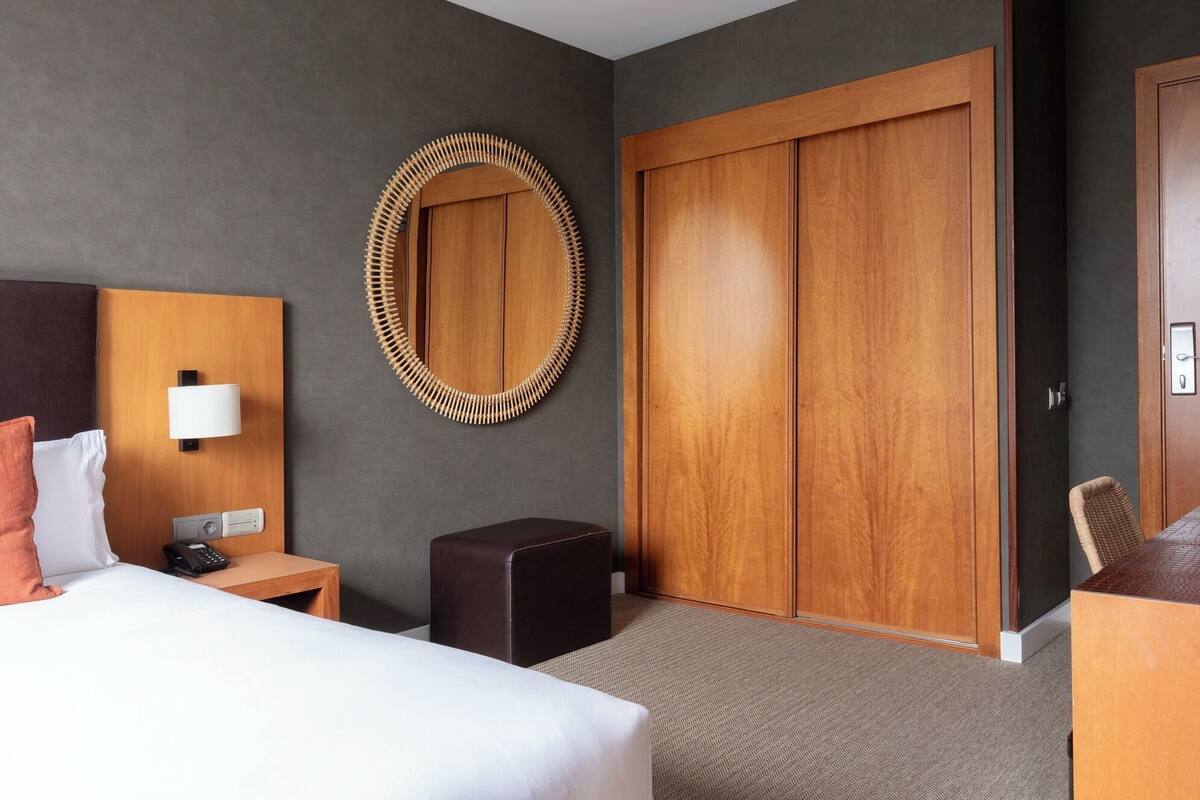 A hotel room with a bed, bedside table, lamp, and a large wooden wardrobe.