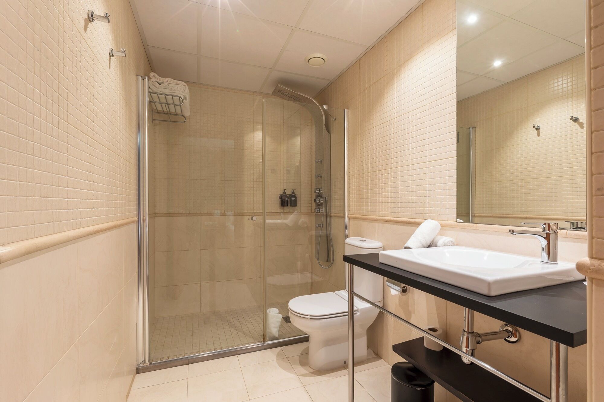 A modern bathroom with a glass-enclosed shower, a white toilet, and a black countertop with a white sink.