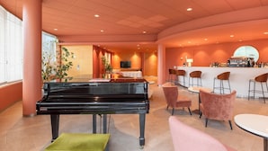 Un espace lounge moderne doté d’un grand piano, de sièges confortables, d’un bar et d’un téléviseur.