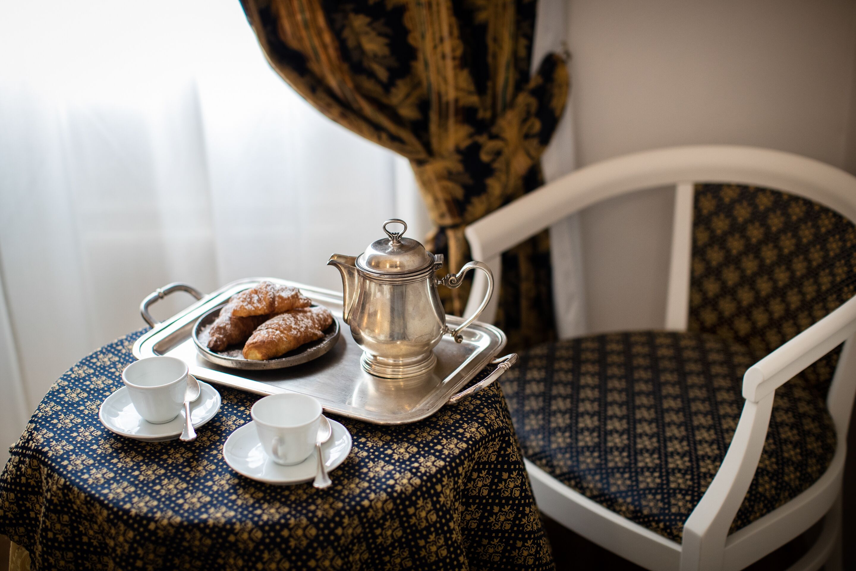 Una mesa con una bandeja que contiene pasteles, un calentador de té y dos tazas con platillos.