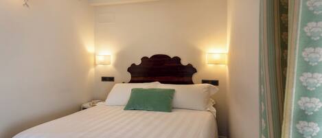 A neatly made bed with white linens and a green pillow, flanked by two wall-mounted lamps.