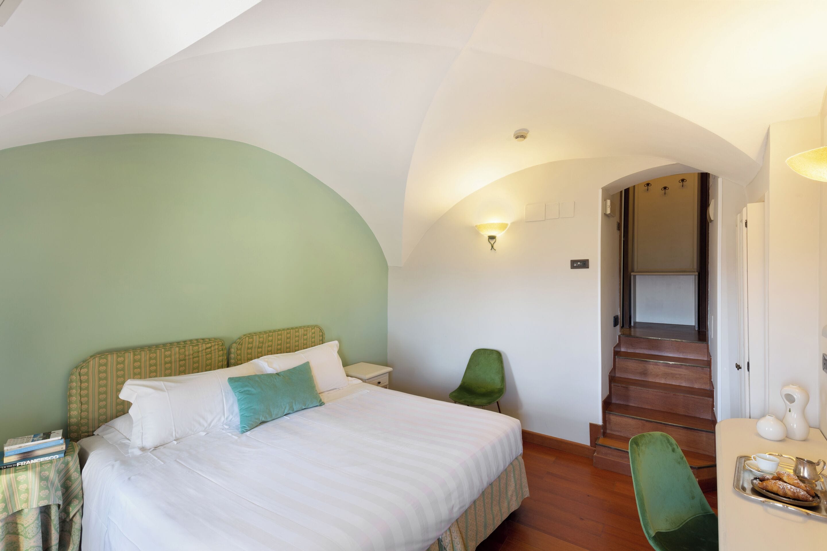 A bedroom with a bed, a chair, a nightstand, and a tray with pastries.