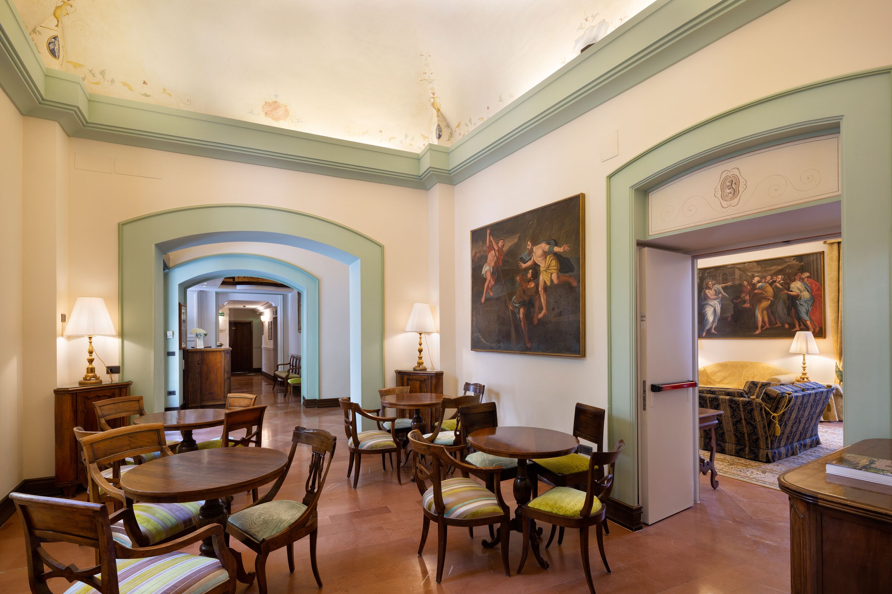 A spacious hotel lobby with a grand staircase, wooden furniture, and classical artwork.