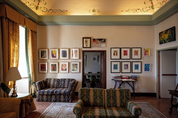 A room with two patterned sofas, a table with books, and framed artworks on the walls.