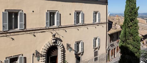 A multi-story building with a beige facade, multiple windows with shutters, and a prominent arched entrance.