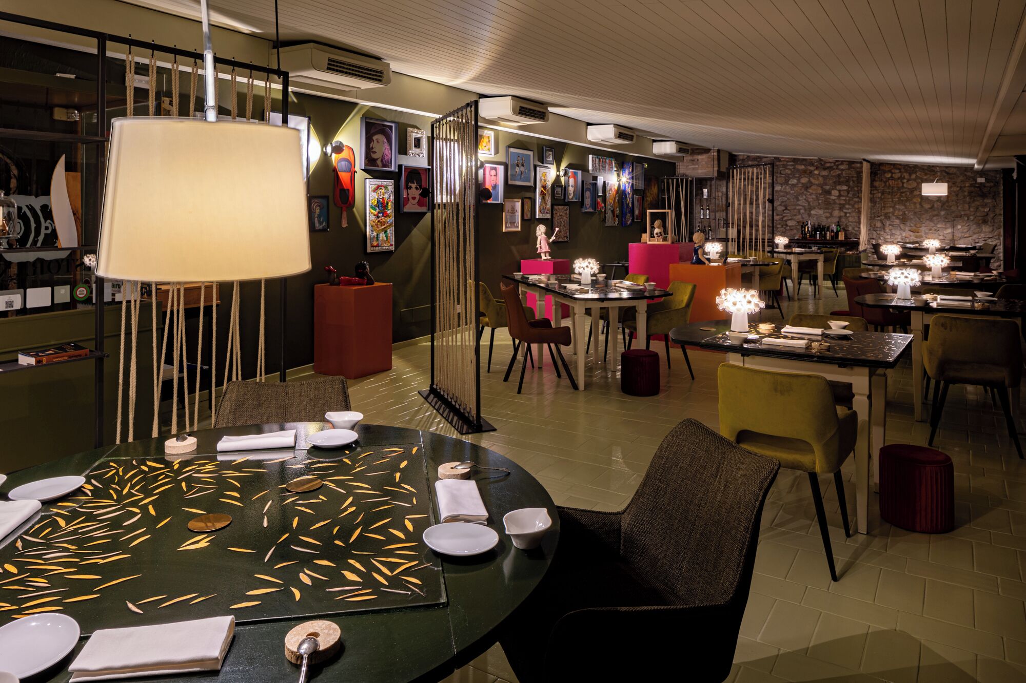 Un restaurante con una mesa redonda para dos comensales, una lámpara colgante y una pared decorada con cuadros.