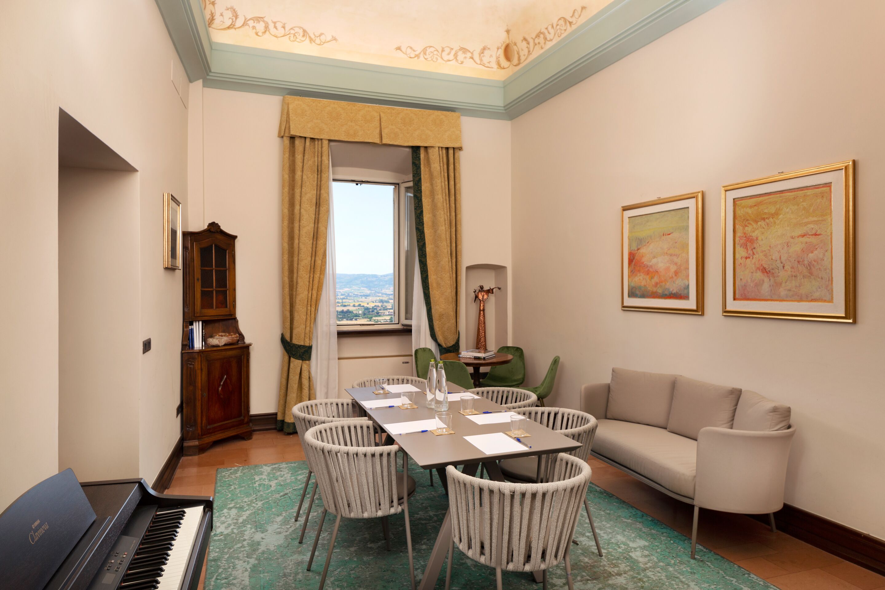 Una habitación con un piano, una mesa de comedor con sillas, un sofá y dos obras de arte enmarcadas en la pared.