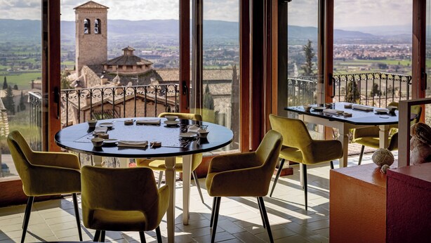 A dining area with a table set for two, overlooking a scenic view of a historic tower and landscape. - Hotel Fontebella (Assisi)