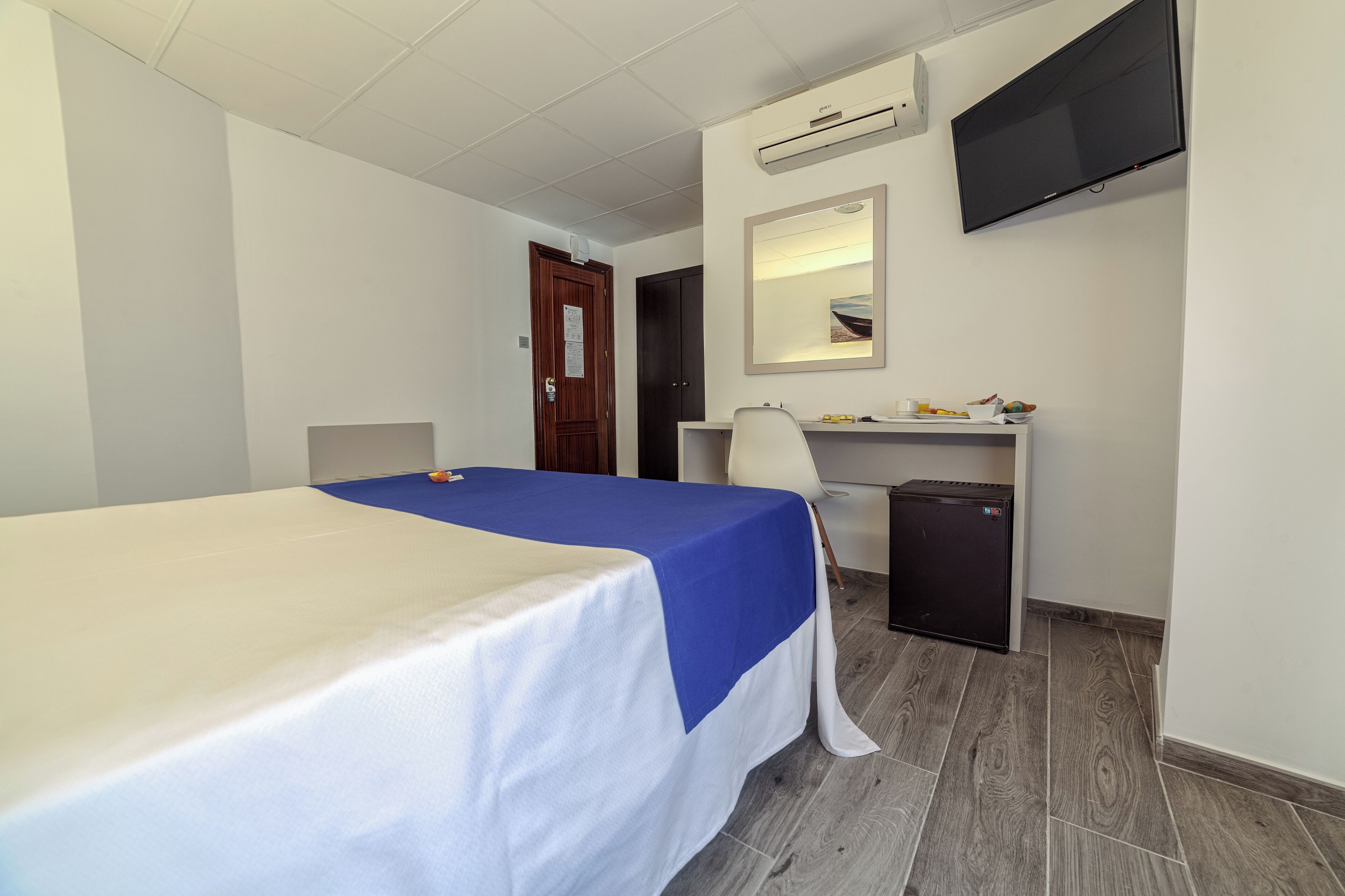 Una habitación de hotel con cama, escritorio, silla y televisión montada en la pared.