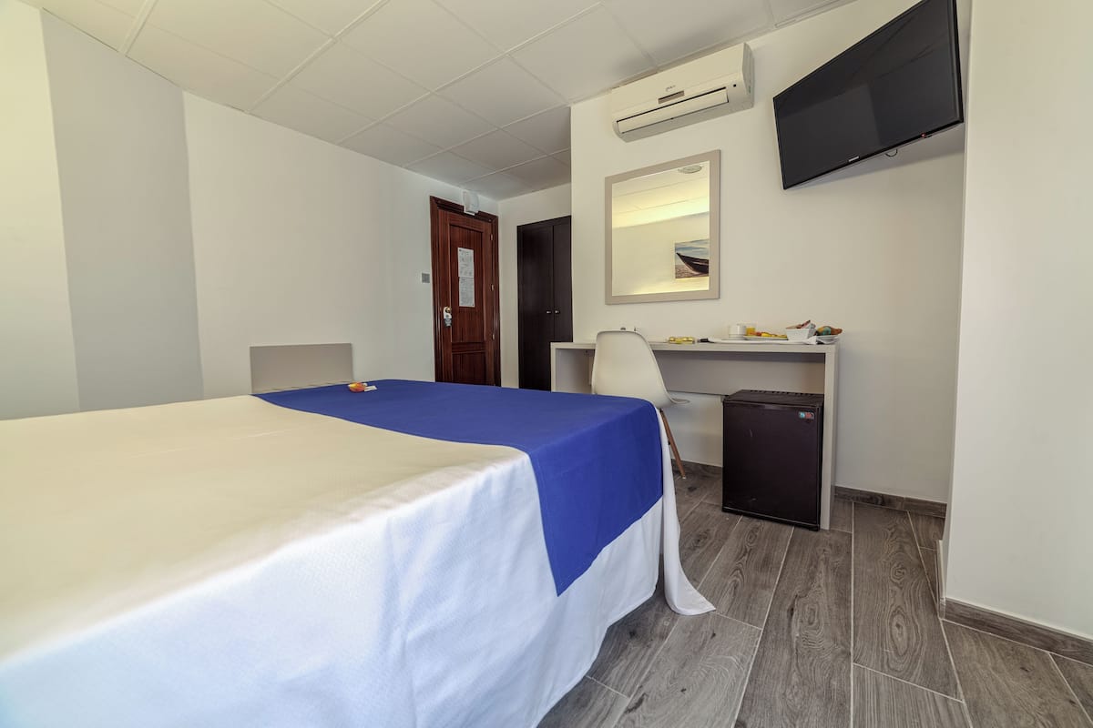 Una habitación de hotel con cama, escritorio, silla y televisión montada en la pared.