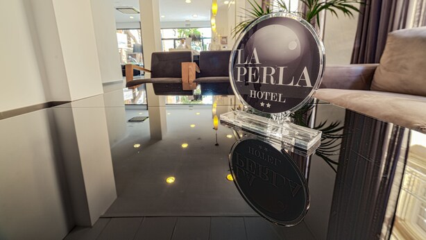 Zona de recepción de un hotel con un escaparate de vidrio, un mostrador de recepción y un área de estar con sofás.