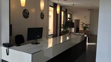 A reception desk with a computer monitor, a telephone, and a potted plant.