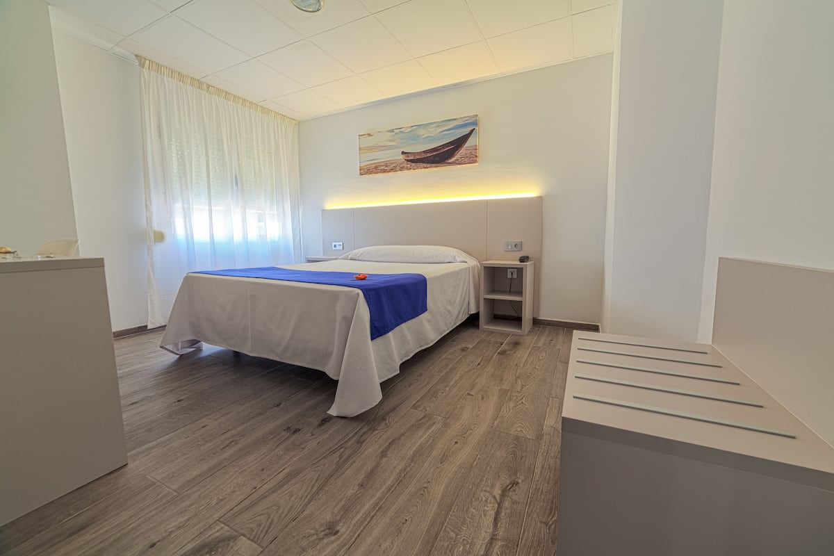 A hotel room with a bed, a nightstand, a desk, and a painting on the wall.