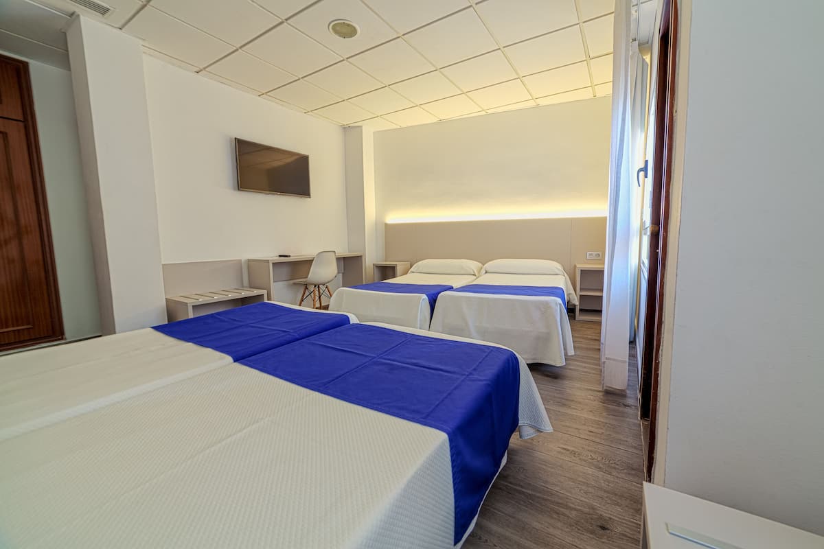 A hotel room with three beds, a TV mounted on the wall, and a wooden floor.