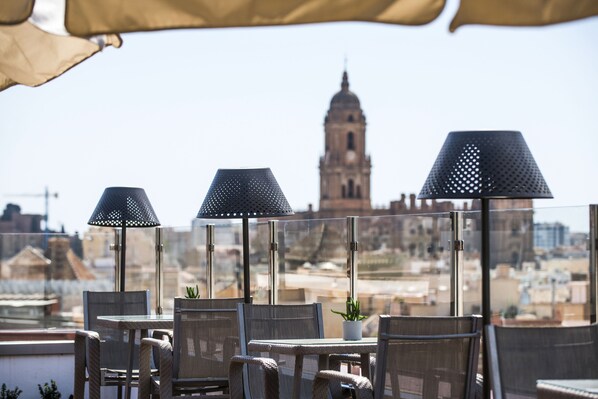 Una terraza en la azotea con mobiliario exterior, vista a una torre histórica y cielo despejado.